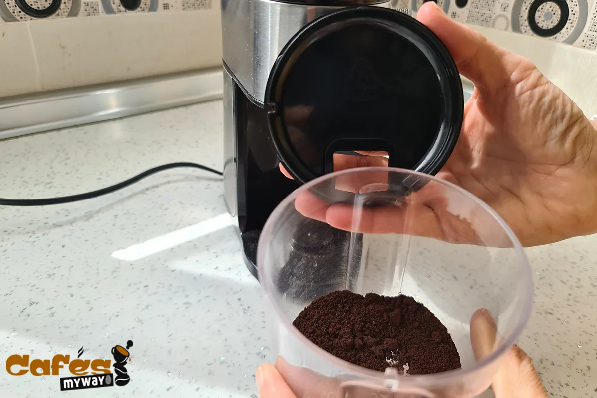 Manos sosteniendo un recipiente transparente con café molido y su tapa fuera del molinillo