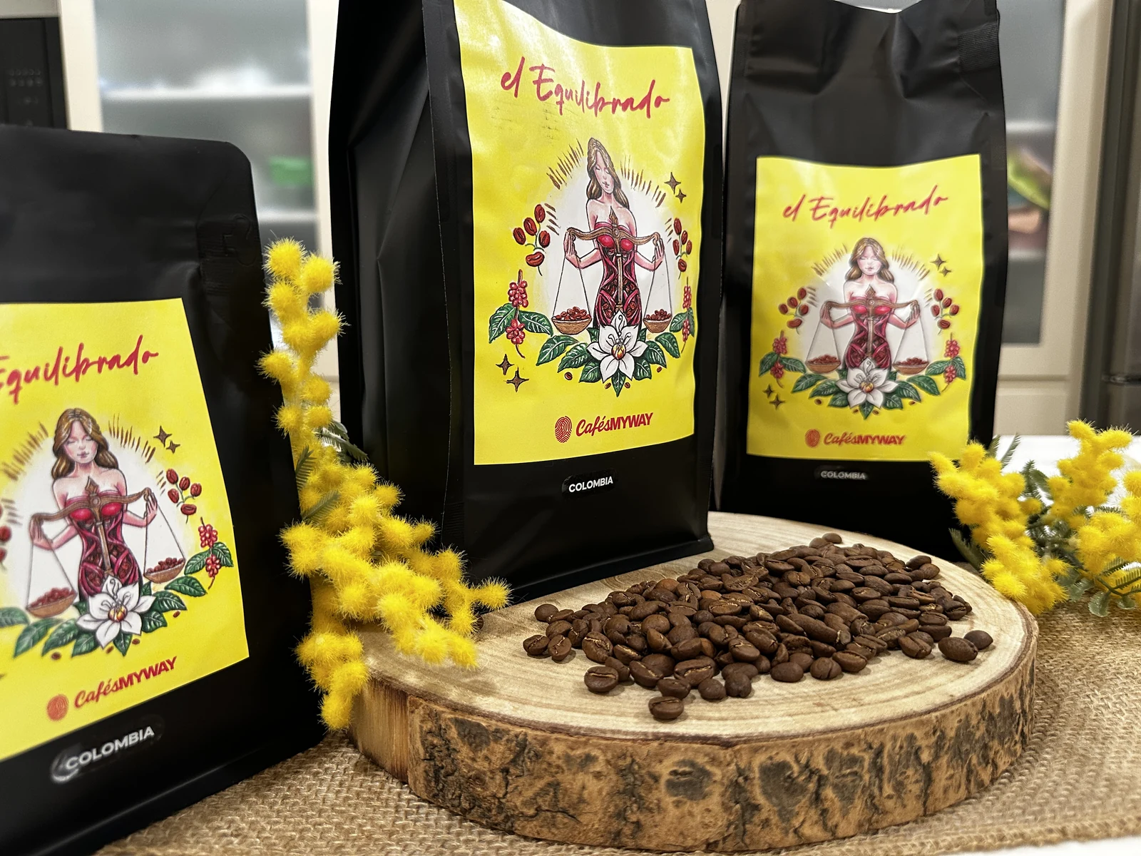 Granos de café sobre una base de madera delante de bolsas de El Equilibrado de Cafés MyWay