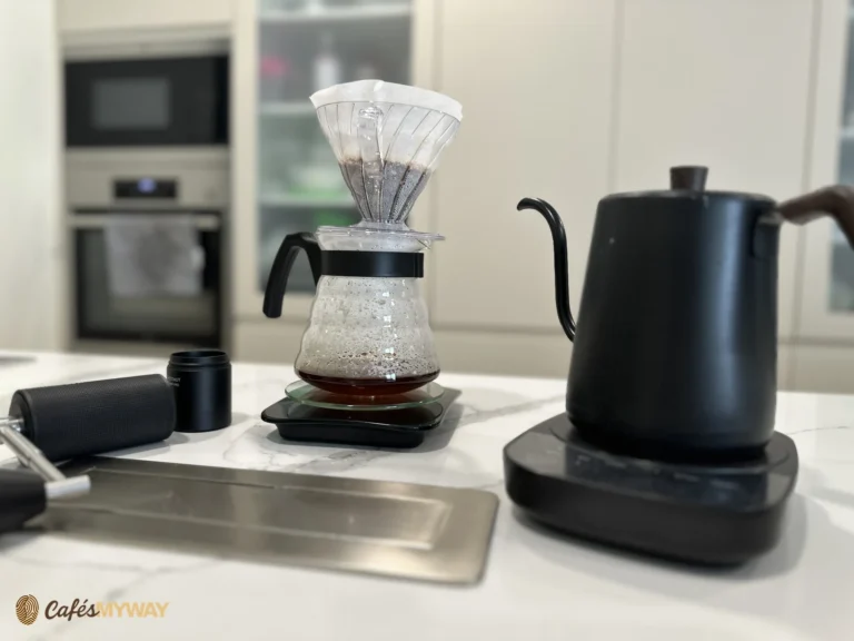 Cono de filtrado con papel sobre una jarra de café junto a un hervidor y un molinillo
